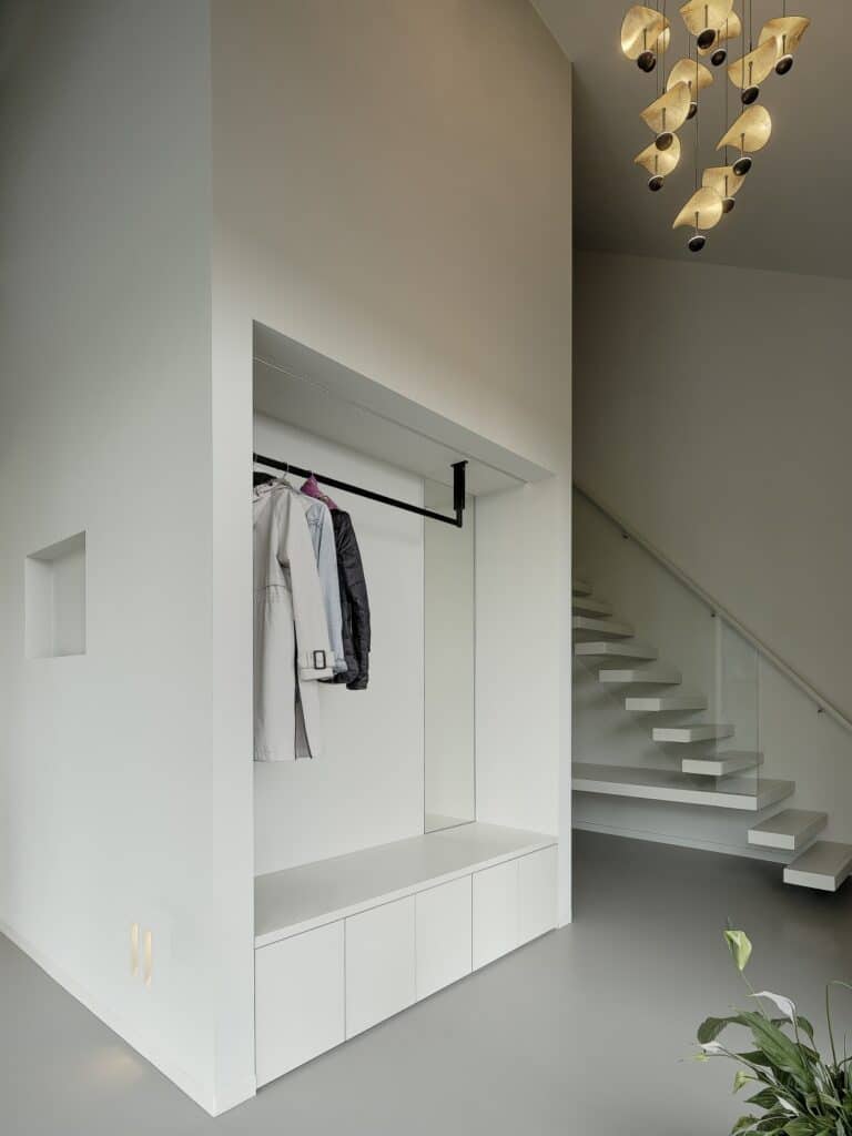 Ingebouwde garderobe met zitbank en spiegel in een lichte entree met zwevende trap