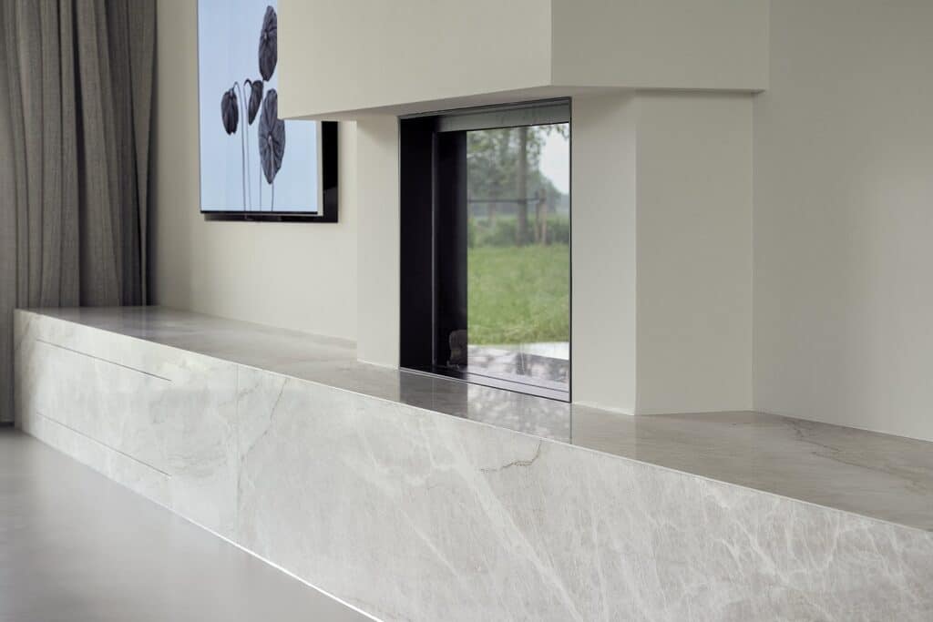 Lang natuurstenen zitmeubel met geïntegreerde haard en opberglades, onderdeel van interieur in De Friese Meren.