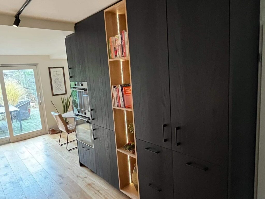 Zwarte houten kast in Drachten met dubbele inbouwoven, open boekenvak en veel opbergruimte op maat.