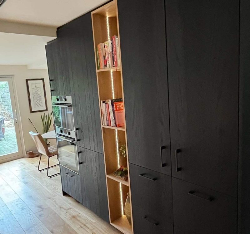 Zwarte houten kast in Drachten met dubbele inbouwoven, open boekenvak en veel opbergruimte op maat.