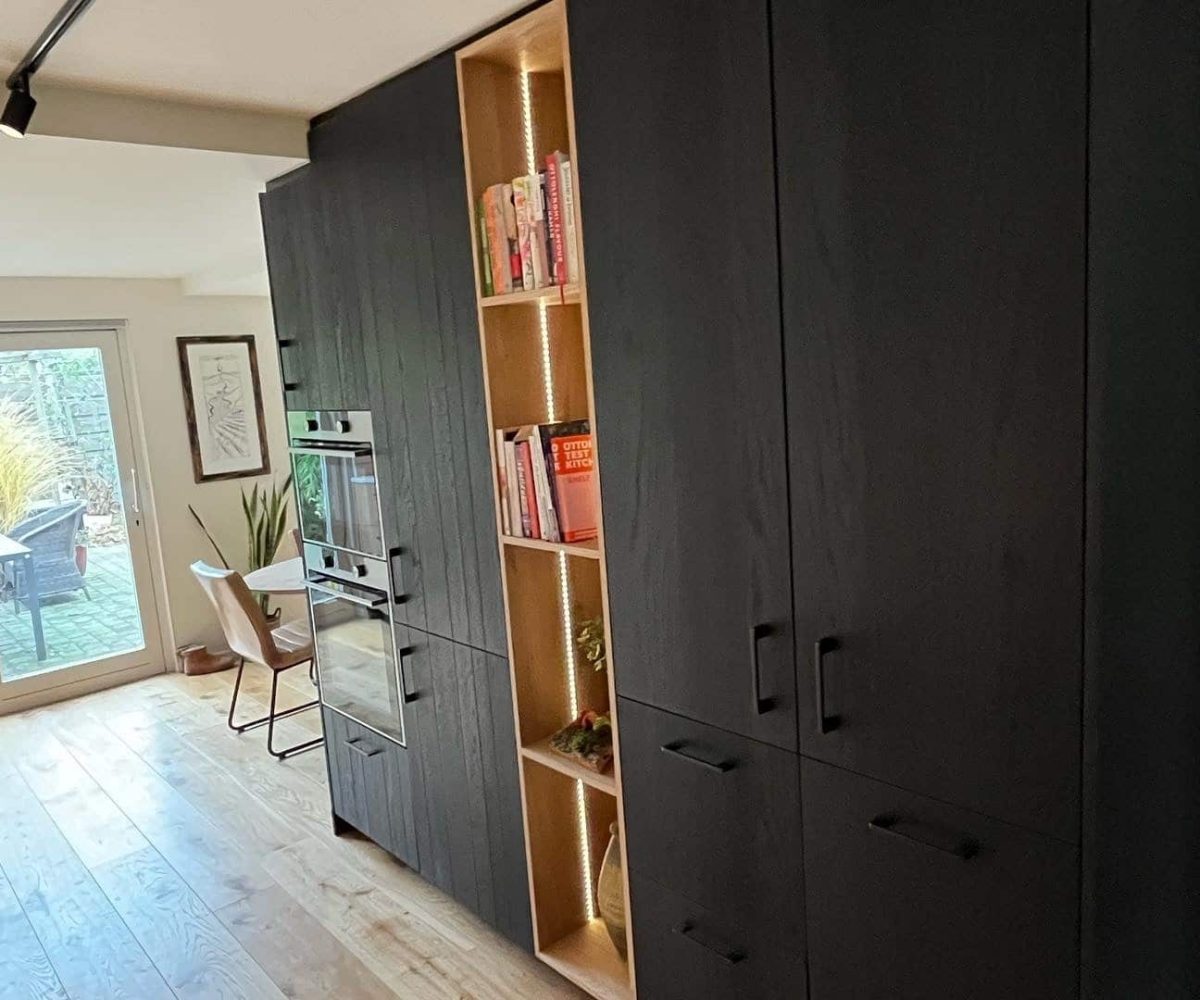 Zwarte houten kast in Drachten met dubbele inbouwoven, open boekenvak en veel opbergruimte op maat.