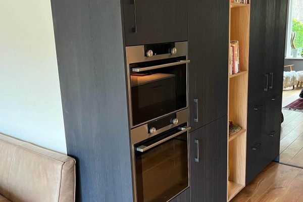 Op maat gemaakte keukenkast in Drachten met zwarte fronten, open nis met verlichting en geïntegreerde oven.