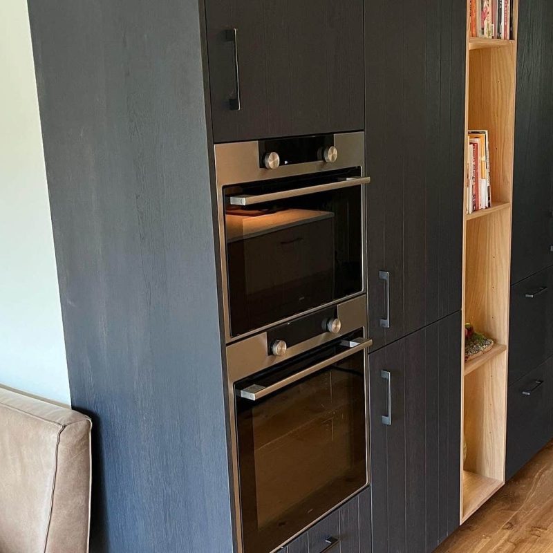 Op maat gemaakte keukenkast in Drachten met zwarte fronten, open nis met verlichting en geïntegreerde oven.