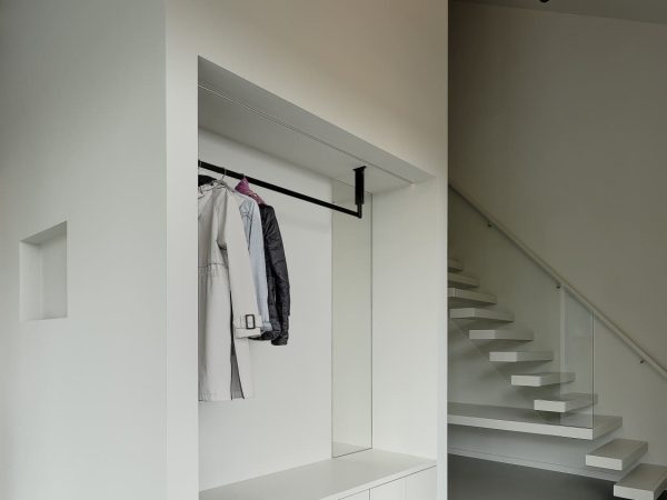 Ingebouwde garderobe met zitbank en spiegel in een lichte entree met zwevende trap
